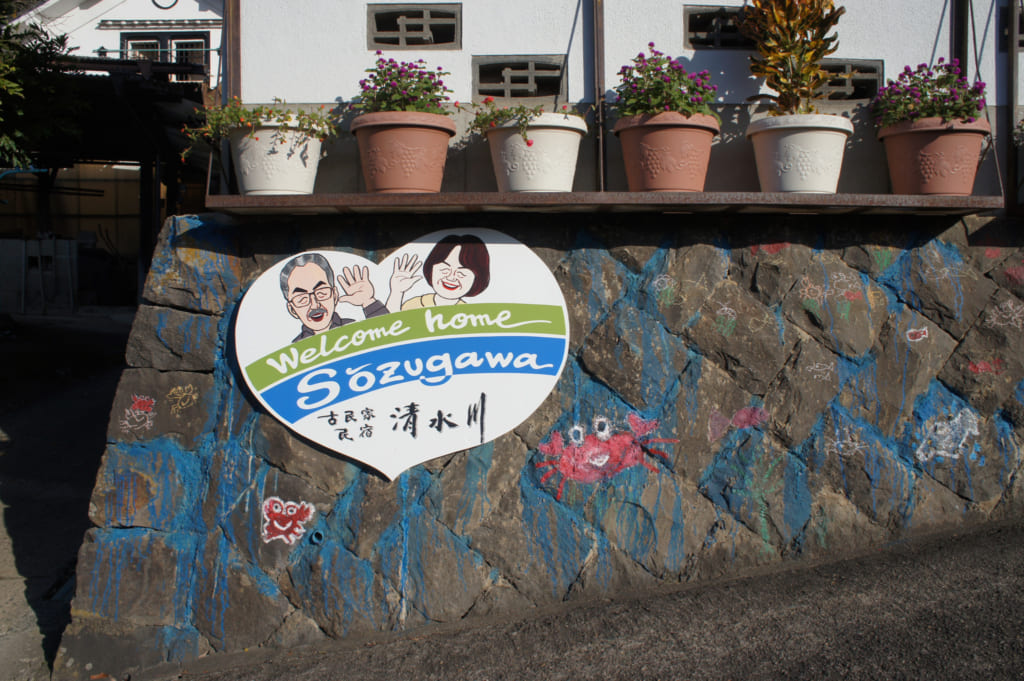 Pancarte sur laquelle une illustration montre le couple Yonemura, devant leur maison