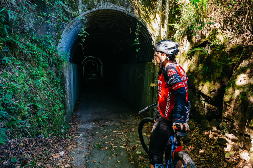 Abe san devant l'entrée d'un étroit tunnel, traversé lors des promendes à vélo à Aso