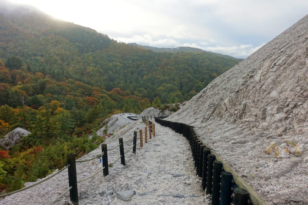 Un chemin de pierres blanches du kawarage jigoku s'étend vers l'horizon au milieu des montagnes verdoyantes de la préfecture d'Akita