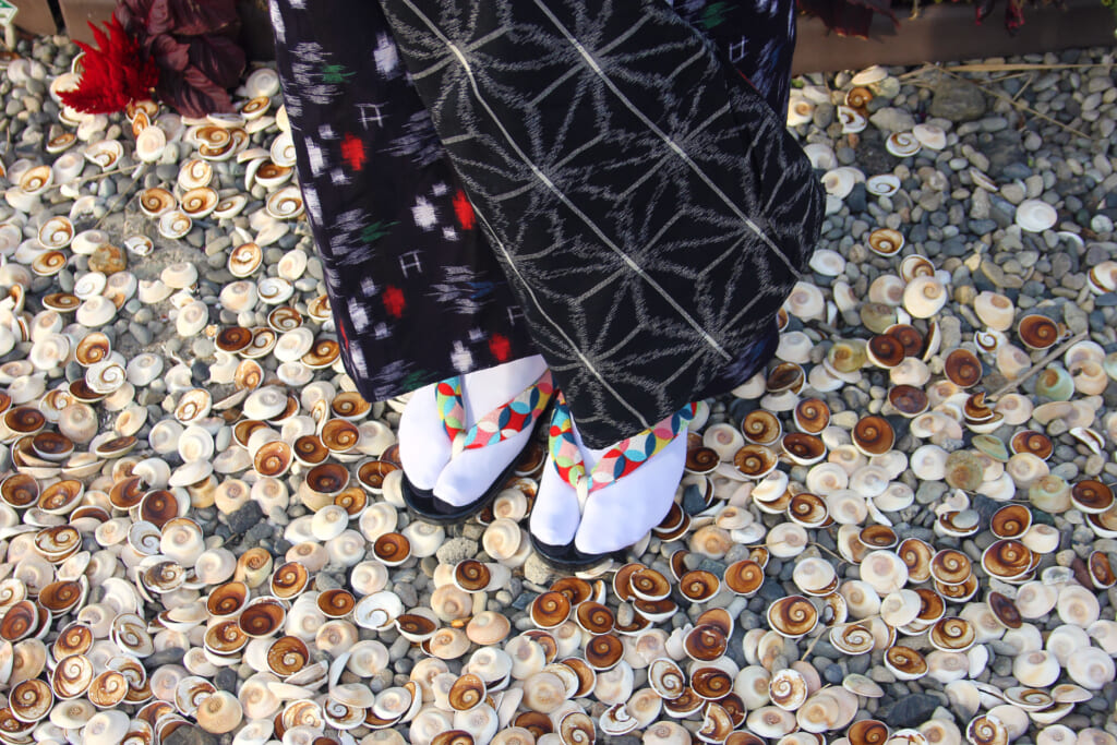 Someone is standing on a floor covered by sea shells, we only see se foot of the person and the bottom of her skirt