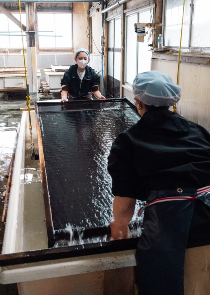 Deux artisanes manient les outils leur permettant de fabriquer une grande feuille de papier washi