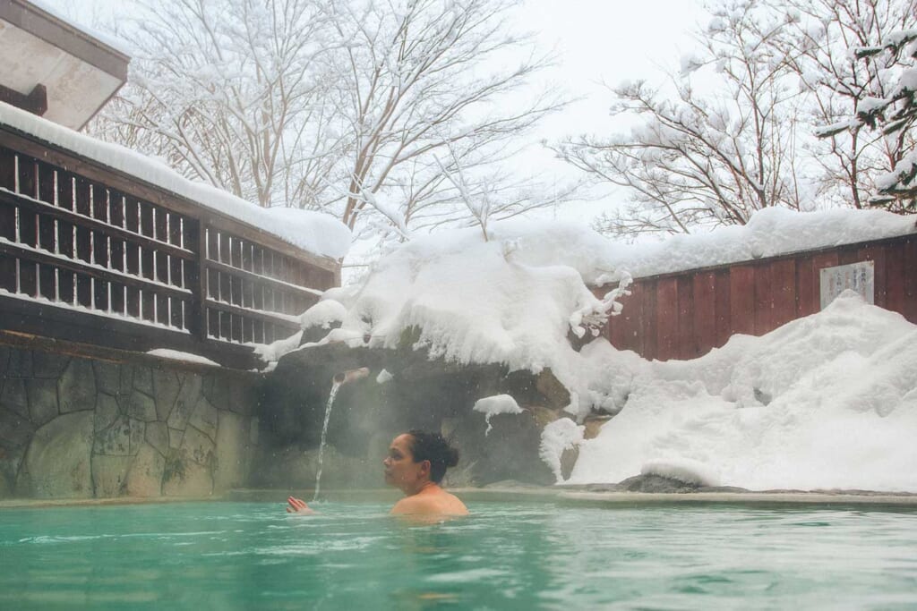 Une jeune femme se baigne dans un onsen japonais entouré de neige