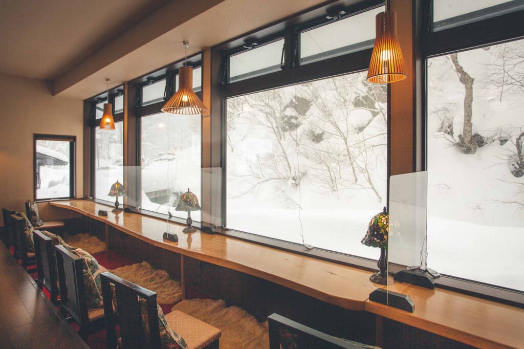 Tables d'un établissement onsen japonais face à de grandes fenêtres sur des paysages enneigés