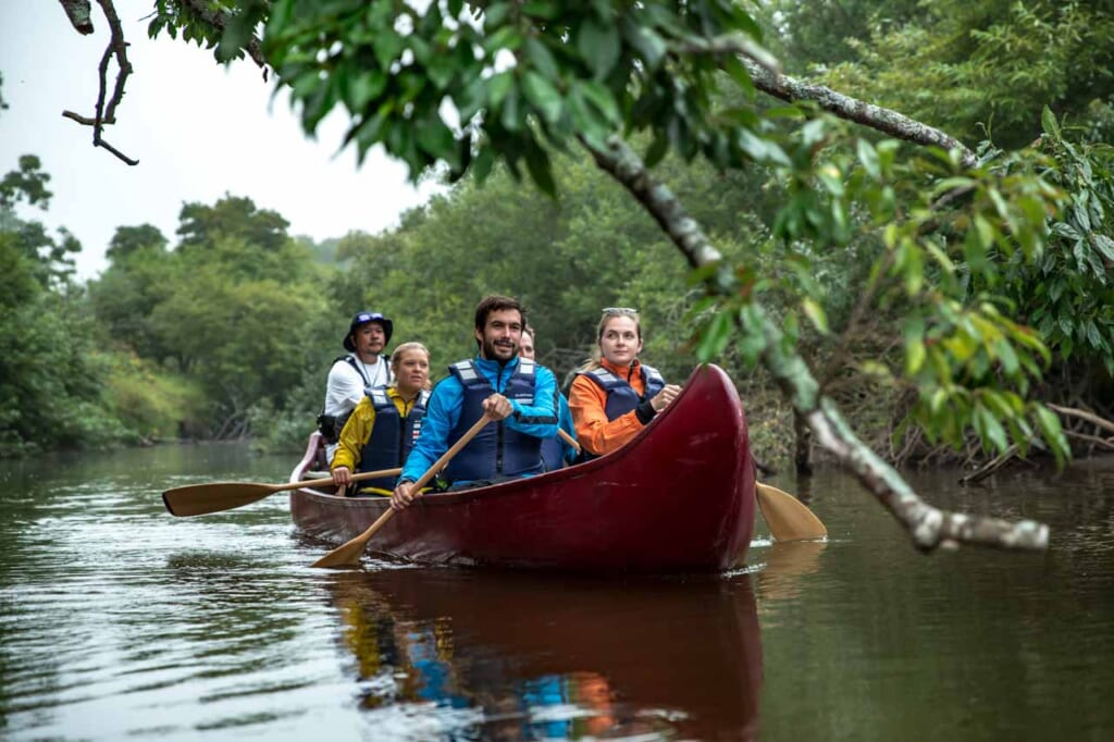 Un groupe de voyageurs fait du canoë sur une rivière entourée de végétation luxuriante à Hokkaido