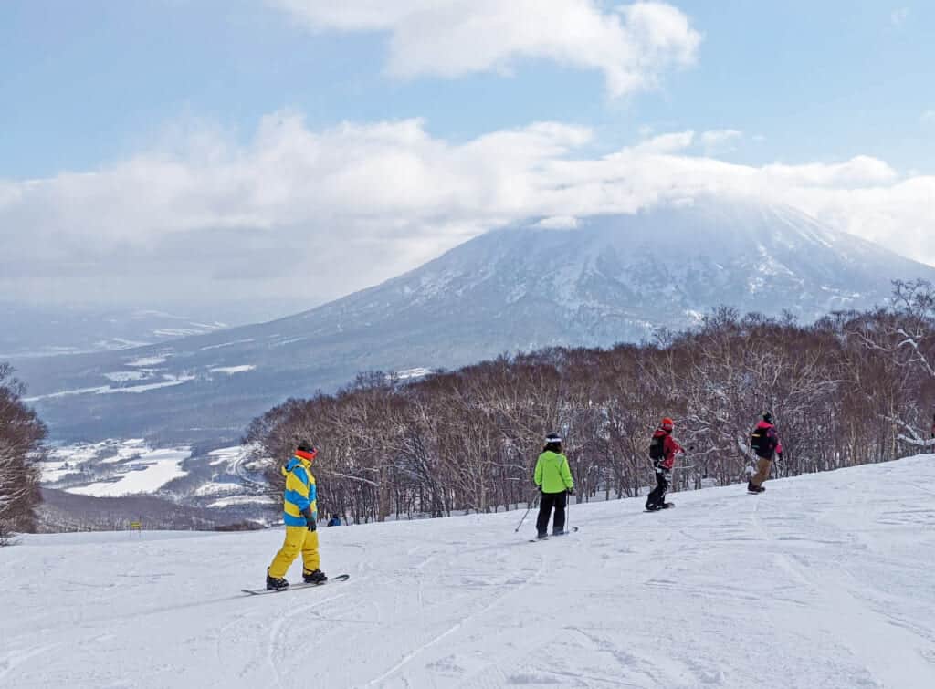 Un groupe en ski et en snowboard sur des pistes de ski dégagées à Hokkaido avec vue sur le mont Yotei