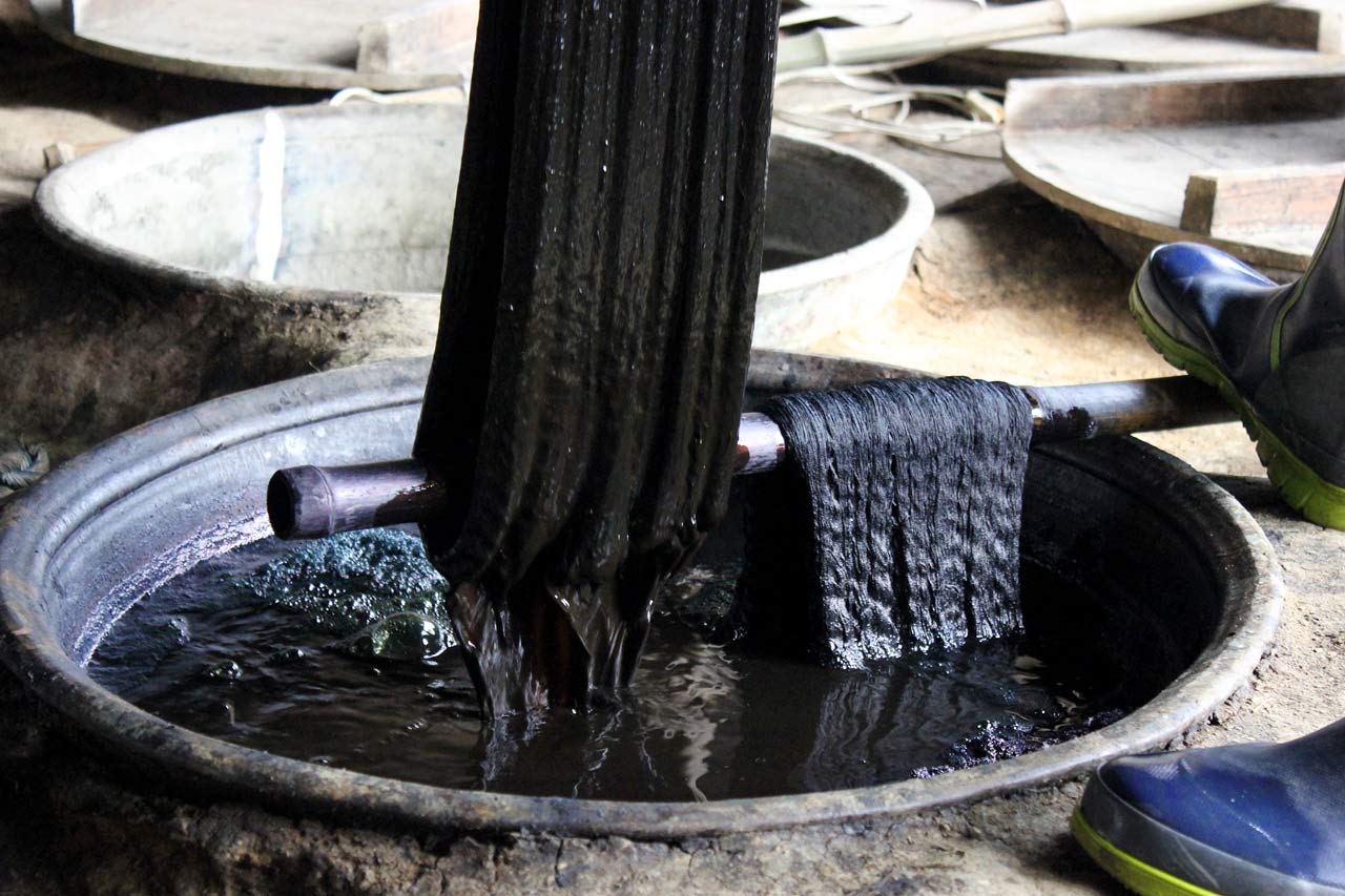 Un fabricant de Kurume kasuri de Hirokawa trempe des fils dans une cuve d'indigo naturel.