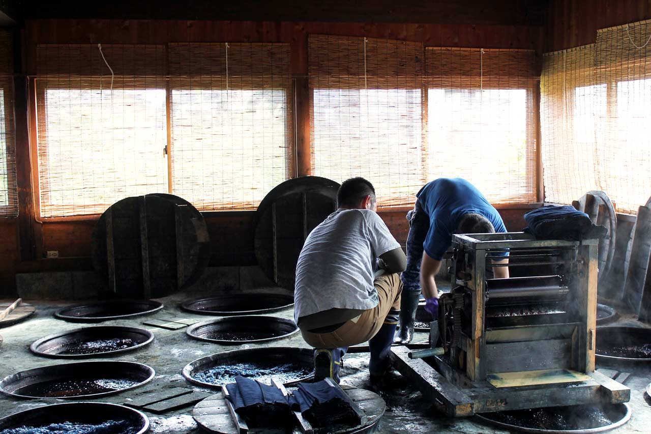 Deux hommes sont en train de plonger des tissus dans des cuves d'indigo à l'atelier Ikeda Kasuri Kobo, Chikugo.