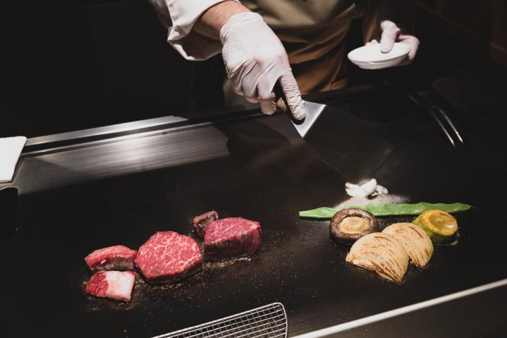 Chef japonaise préparant du bœuf wagyu et des légumes sur une plaque  chauffante teppanyaki