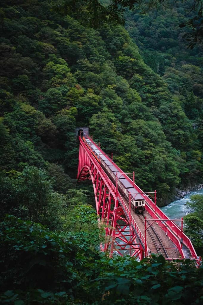 Train torokko des gorges de Kurobe qui traverse un pont métallique rouge