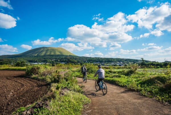 2 personnes à vélo sur un chemin rural devant le mont Onidake à Goto