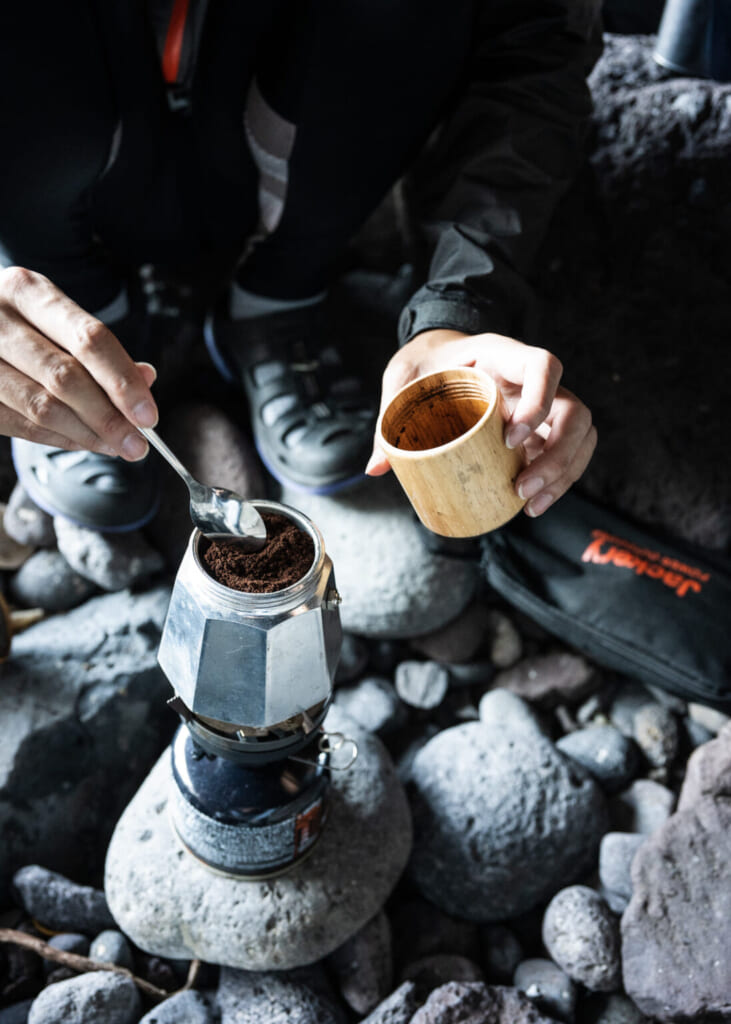 mains qui préparent un pot de café dehors sur des pierres