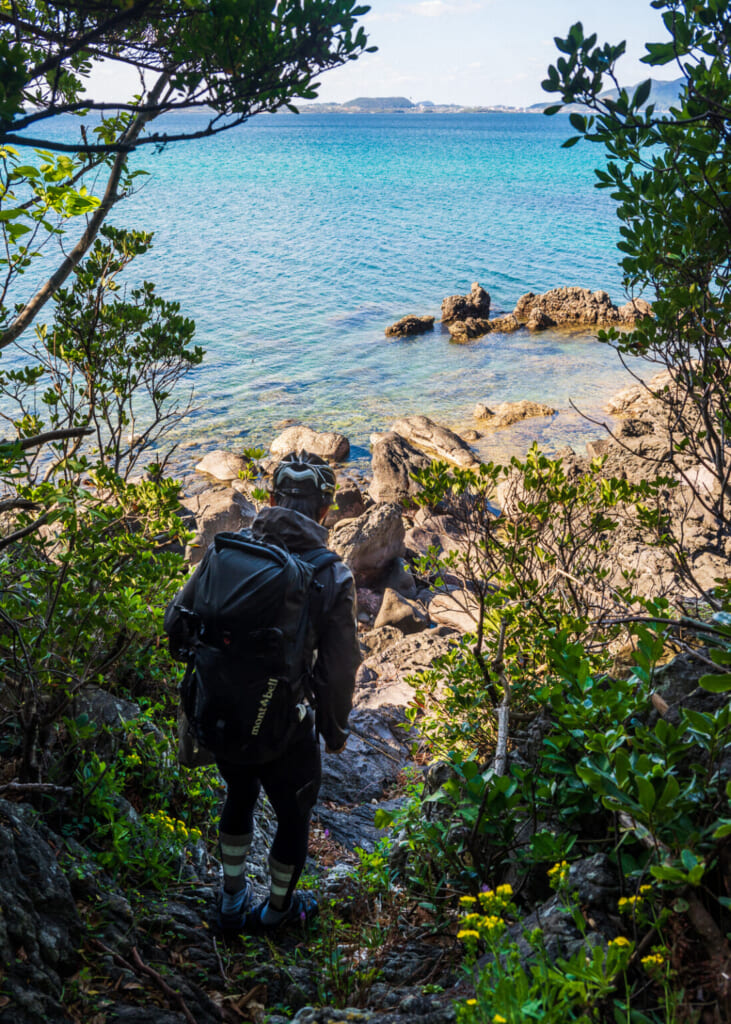 personne qui descend un chemin embroussaillé vers la côte rocheuse dans les îles Goto