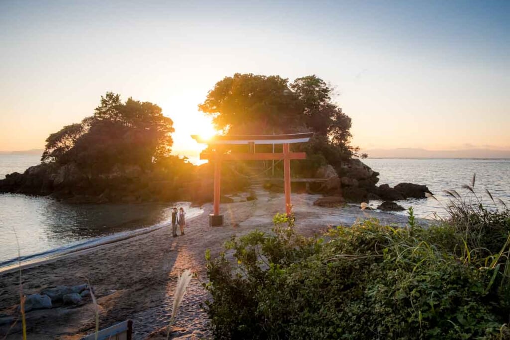 Un couple près d'un sanctuaire japonais en bord de mer durant le coucher du soleil