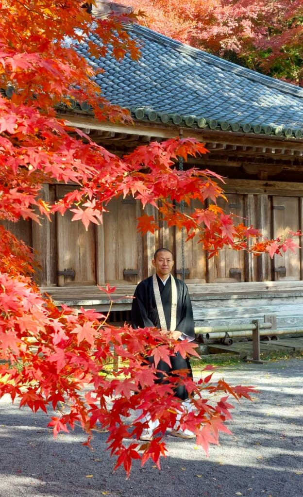 Un moine bouddhiste japonais devant un temple avec des érables japonais en automne