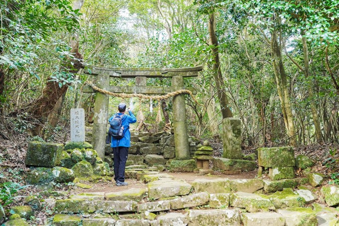 Une personne prend une photo devant un torii de pierre au Japon, dans un chemin de montagne