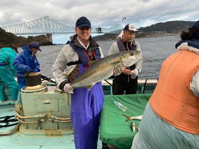 Un homme ayant pêché un poisson qu'il tient dans ses mains, sur un bateau au Japon