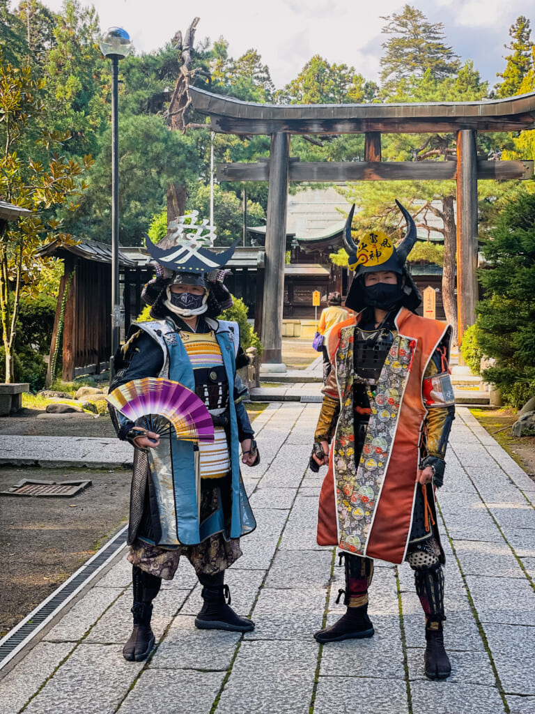 dos personas vestidas de samurai delante de una puerta torii