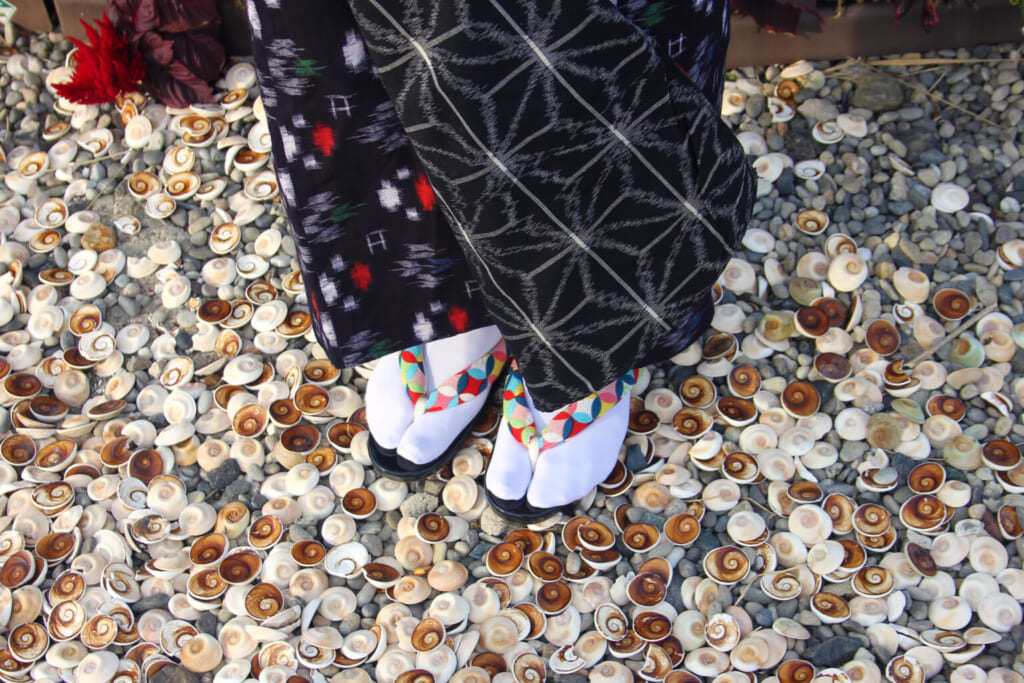 Una mujer vestida con kimono encima de caparazones de caracoles marinos