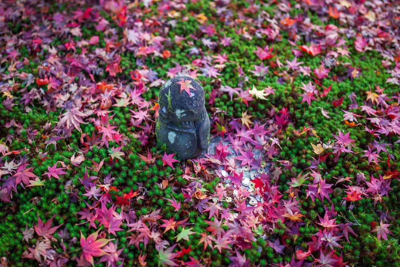 Steinfigur mit roten Ahornblättern, Momiji, in Japan.